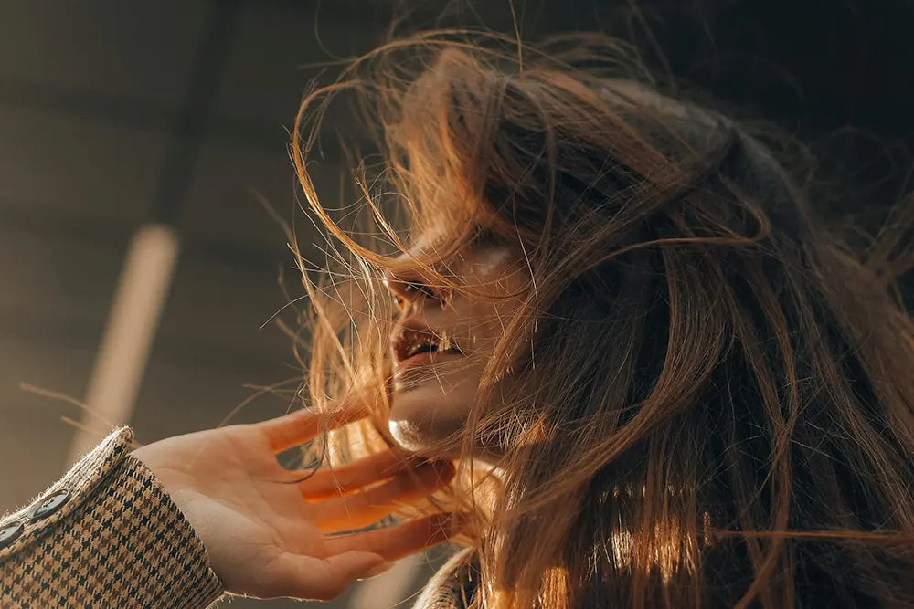 femme chevelure dans le vent rousse main qui touche son menton comment avoir une chevelure saine et brillante